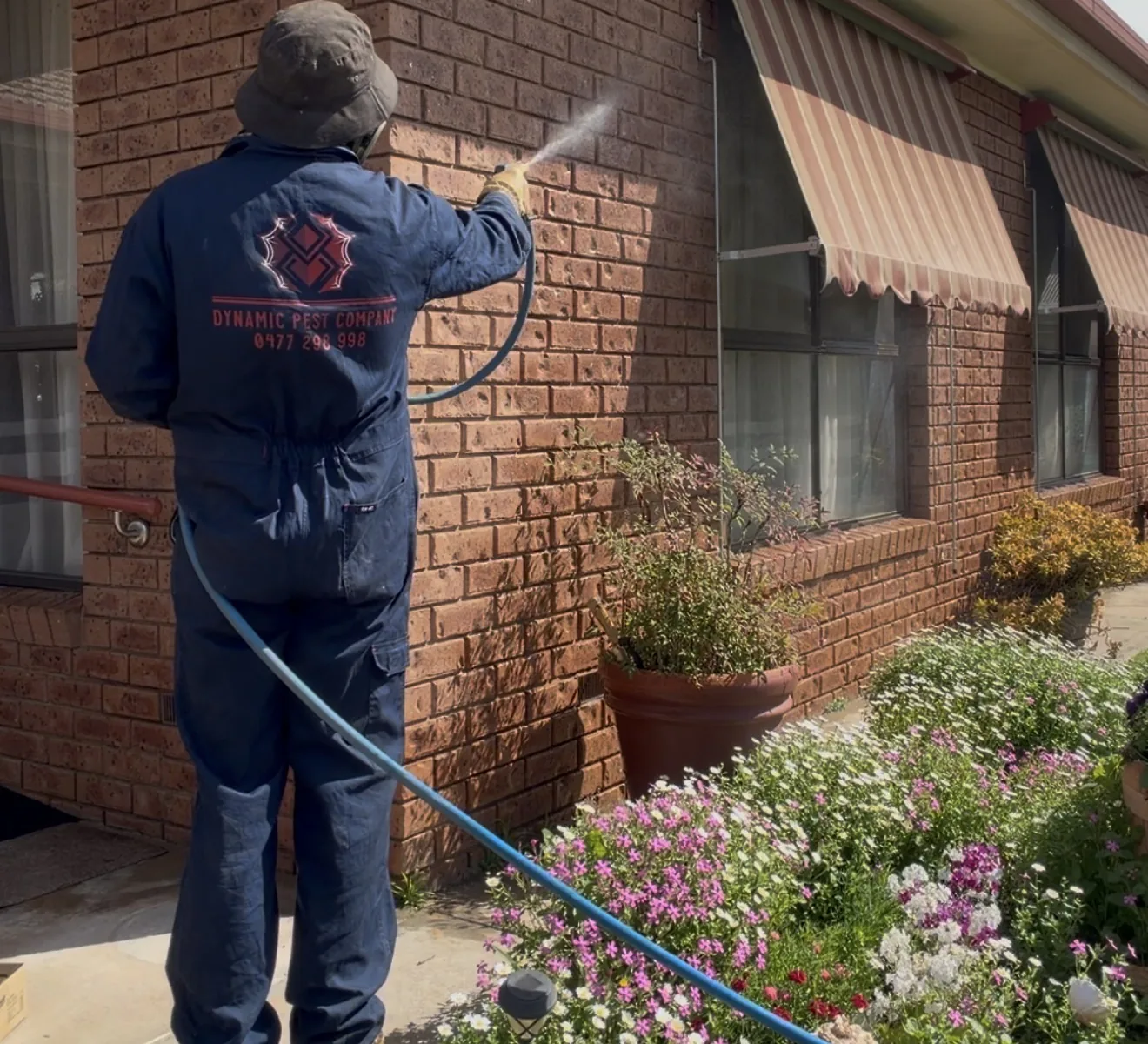 Dynamic Pest Company technician applying a perimeter pest treatment to a brick home